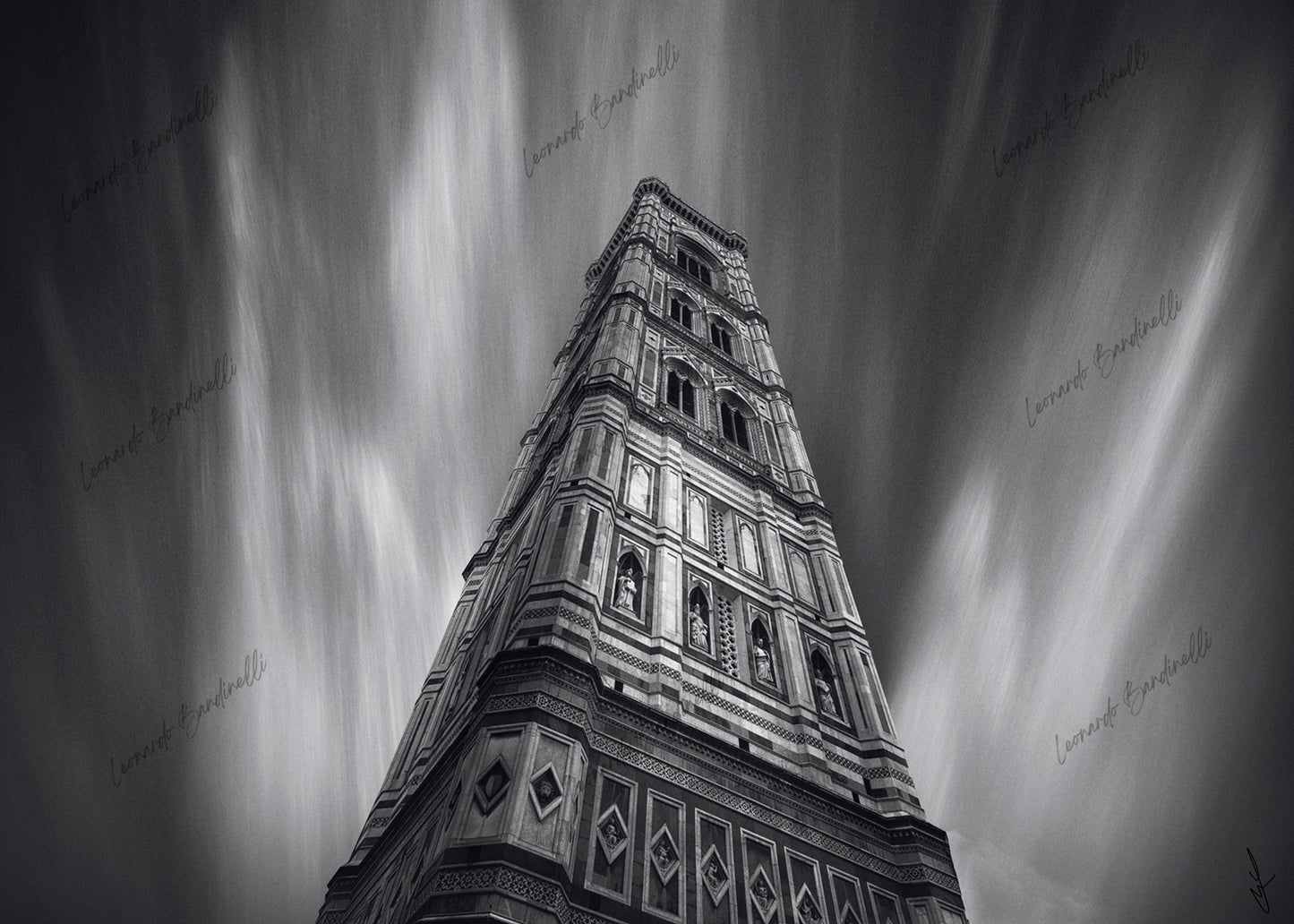 Fotografia fine art in bianco e nero del Campanile di Giotto a Firenze, ripreso dal basso con una lunga esposizione che crea scie verticali nel cielo, enfatizzando la monumentalità della struttura e il contrasto tra architettura e movimento.
Black and white fine art photograph of Giotto’s Bell Tower in Florence, shot from a low angle with long exposure creating vertical light streaks in the sky, emphasizing the monumentality of the structure and the contrast between architecture and motion.