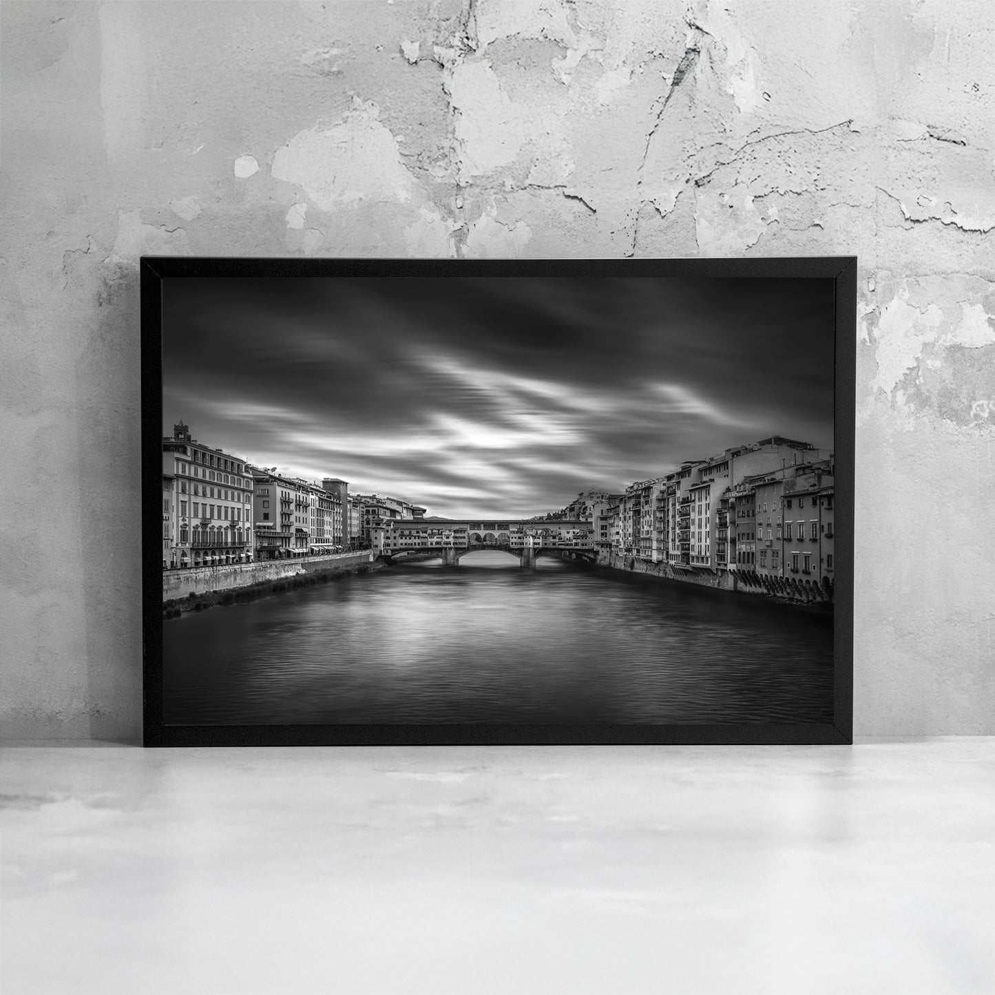 Fotografia fine art in bianco e nero incorniciata di Ponte Vecchio a Firenze, ripreso frontalmente sul fiume Arno con lunga esposizione, presentata come dettaglio di stampa e cornice.
Black and white fine art photograph shown framed of Ponte Vecchio in Florence viewed over the Arno River with long exposure, presented as a print and frame detail.
