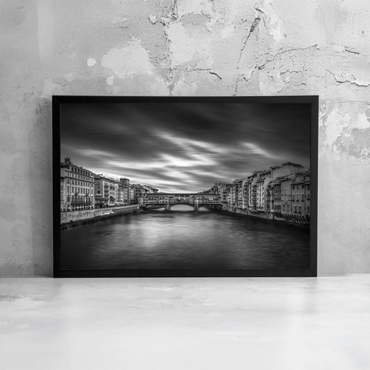 Fotografia fine art in bianco e nero incorniciata di Ponte Vecchio a Firenze, ripreso frontalmente sul fiume Arno con lunga esposizione, presentata come dettaglio di stampa e cornice.
Black and white fine art photograph shown framed of Ponte Vecchio in Florence viewed over the Arno River with long exposure, presented as a print and frame detail.
