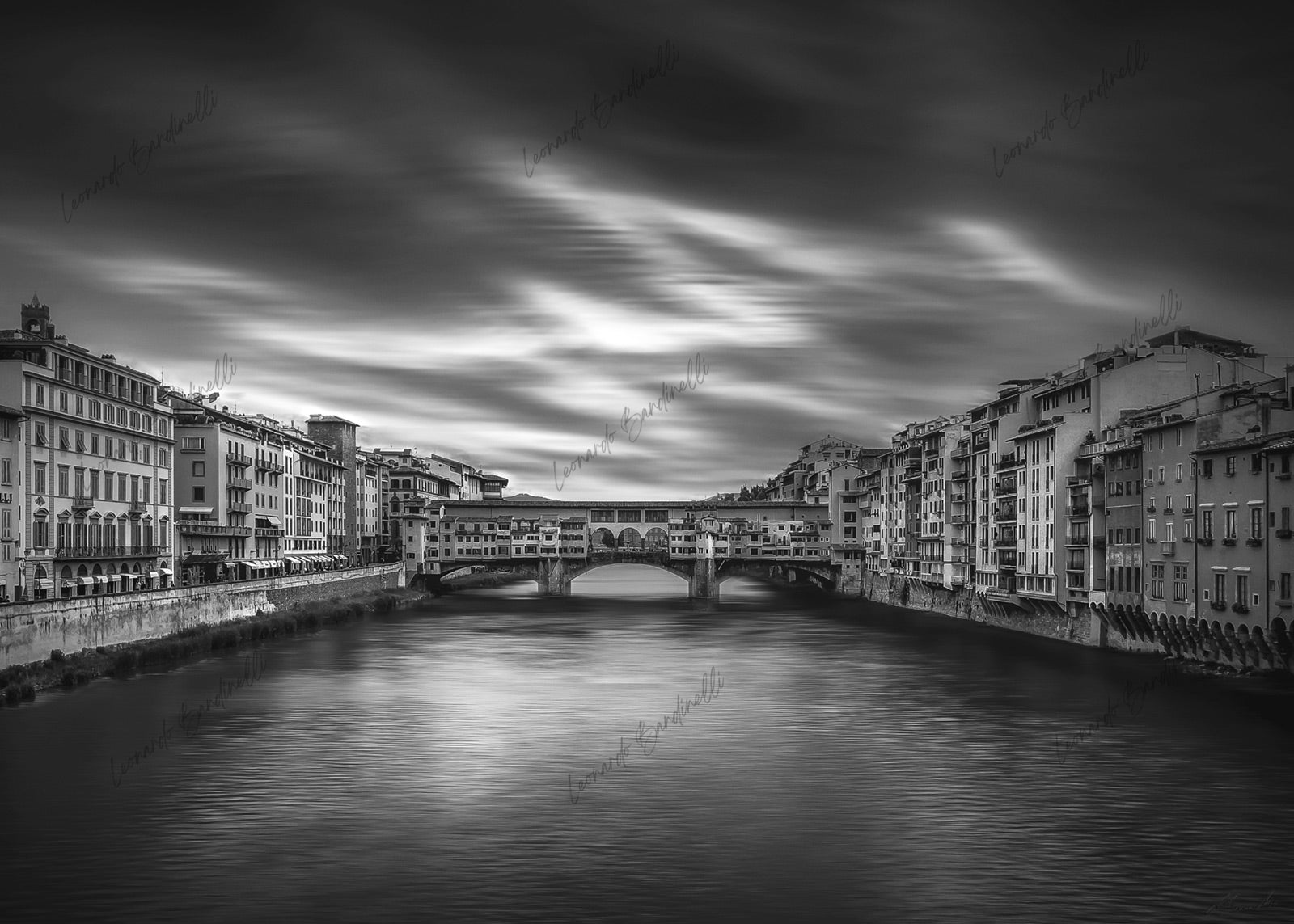 Fotografia fine art in bianco e nero di Ponte Vecchio a Firenze, ripreso frontalmente sul fiume Arno con lunga esposizione che rende l’acqua e il cielo morbidi e sfumati, mentre gli edifici storici restano definiti e simmetrici. Black and white fine art photograph of Ponte Vecchio in Florence, viewed frontally over the Arno River, with long exposure creating smooth water and soft clouds, while the historic buildings remain sharp and symmetrical.